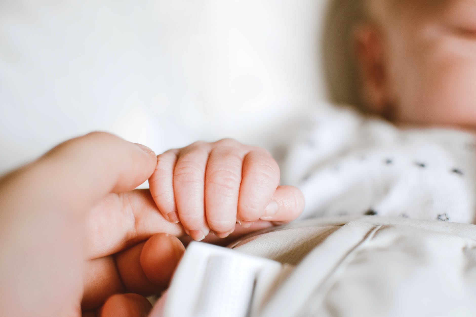 Close up photo of a baby's hand gripping an adult's finger