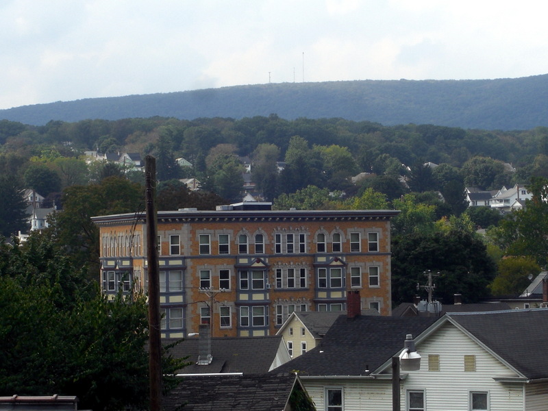 Color photograph of Bangor, Pennsylvania as seen from the surrounding hills, with photo centered on a large brick building surrounded by trees and rooftops