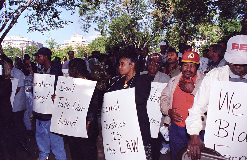 Color photo of a group of Black farmers with signs protesting USDA discrimination at Lafayette Park, 1997