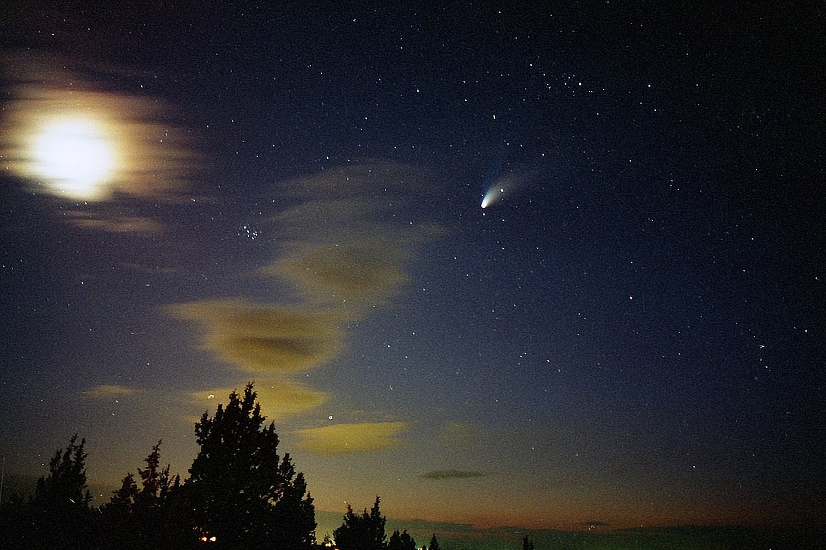 Photograph of Comet Hale-Bopp in night sky, alongside stars, clouds, and blurred moon