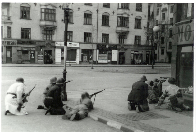 Black-and-white photo of resistance fighters in Copenhagen, crouched on a street corner with guns, 1945