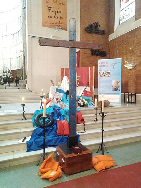 The Lampedusa Cross, made from the wood of a capsized refugee boat, standing on display and surrounded by lit candles