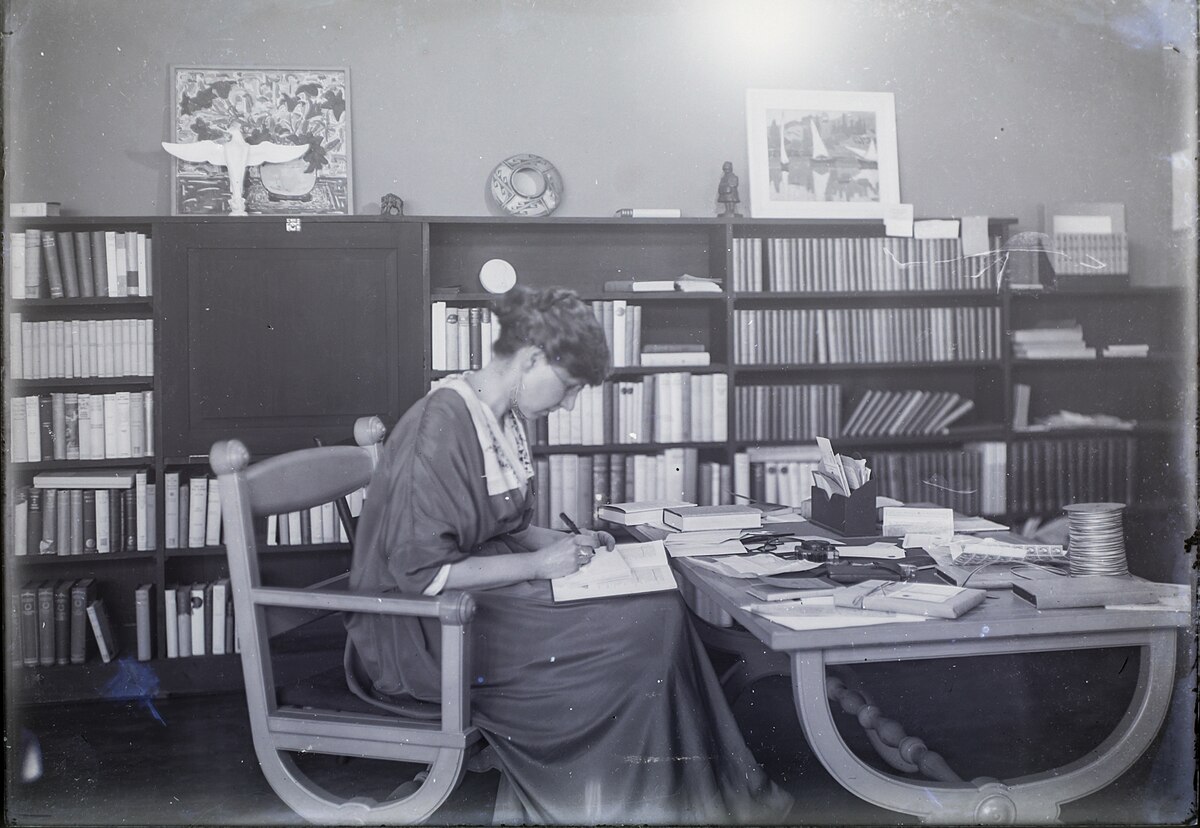 Black and white photo of Madge Jenison sitting at a table in her bookstore reading