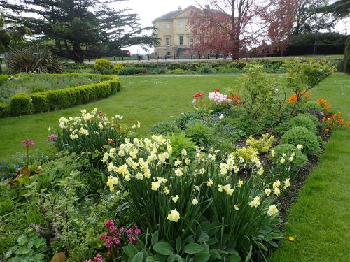 Color photograph of the Old English Garden at Dandon Park in London, showing an expanse of green lawn, flower beds and shrubs, and a mansion in the background