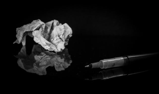 Photo of pen and crumped paper on black reflective surface