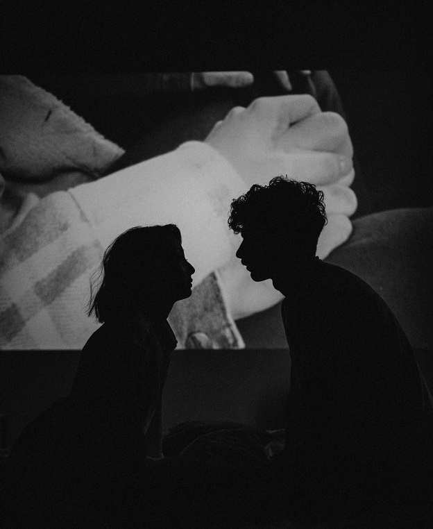 Black and white photo of two young people about to kiss in front of a movie screen