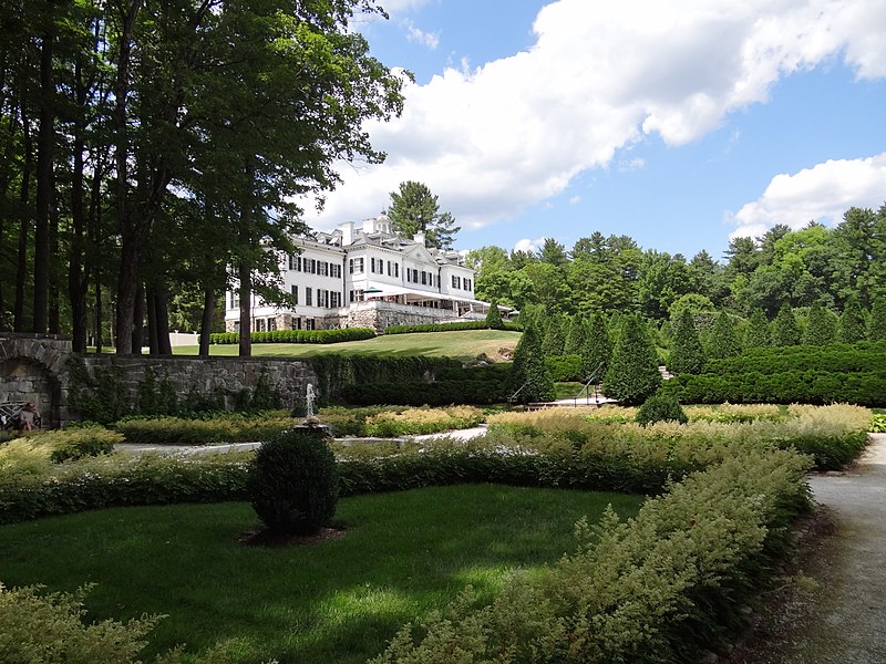 Color photo of Edith Wharton's home, a white mansion surrounded by greenery, taken from a distance across the property grounds